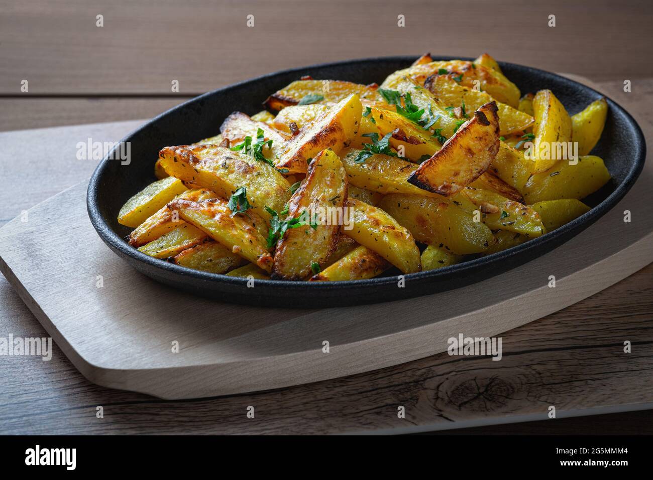 Fried potatoes in a rural style, with spices. On rustic pan, on a wooden table, close view copy space Stock Photo