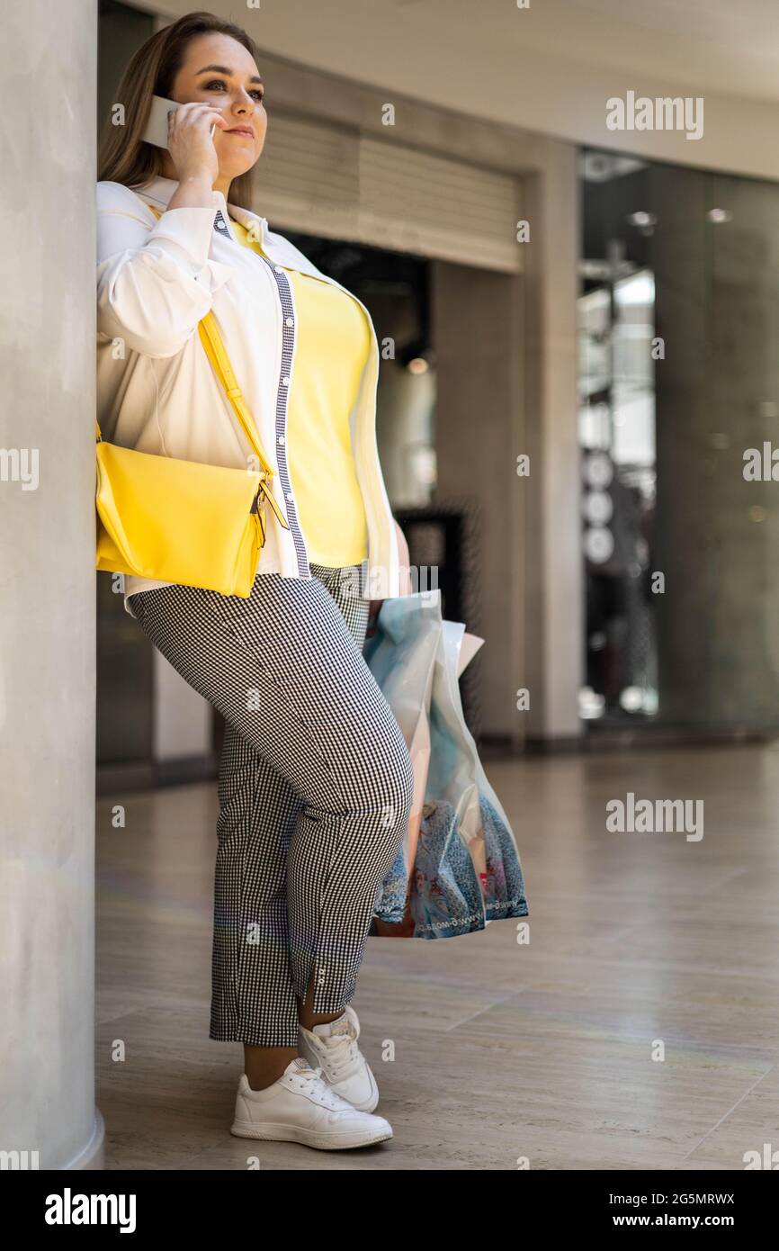 Closeup buyer woman talking smartphone smiling holding bags with purchasing at shopping mall Stock Photo