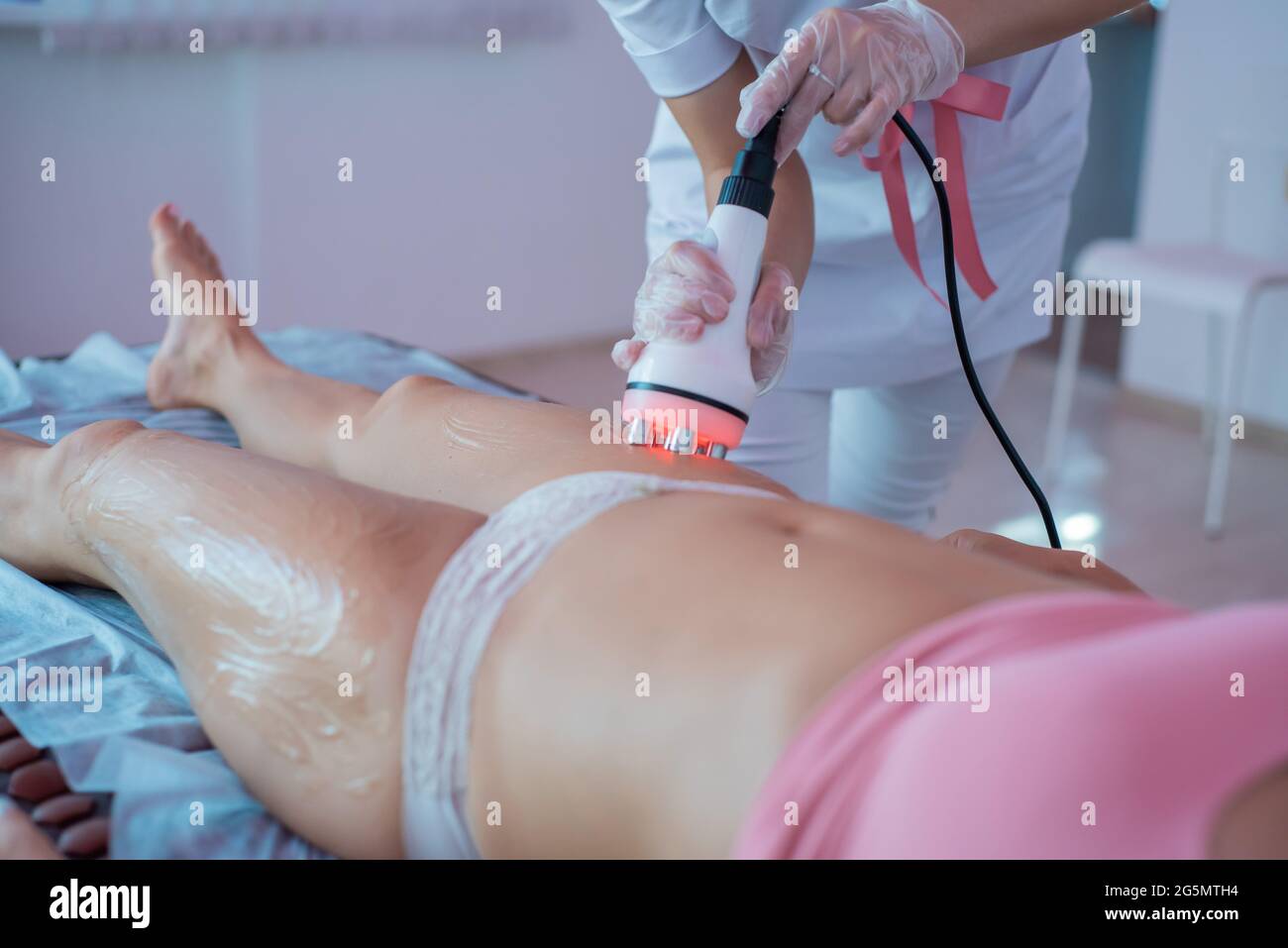 Woman receives an electric massage against cellulite. The doctor performs ultrasonic cavitation correction of the body contours for the patient. Anti Stock Photo