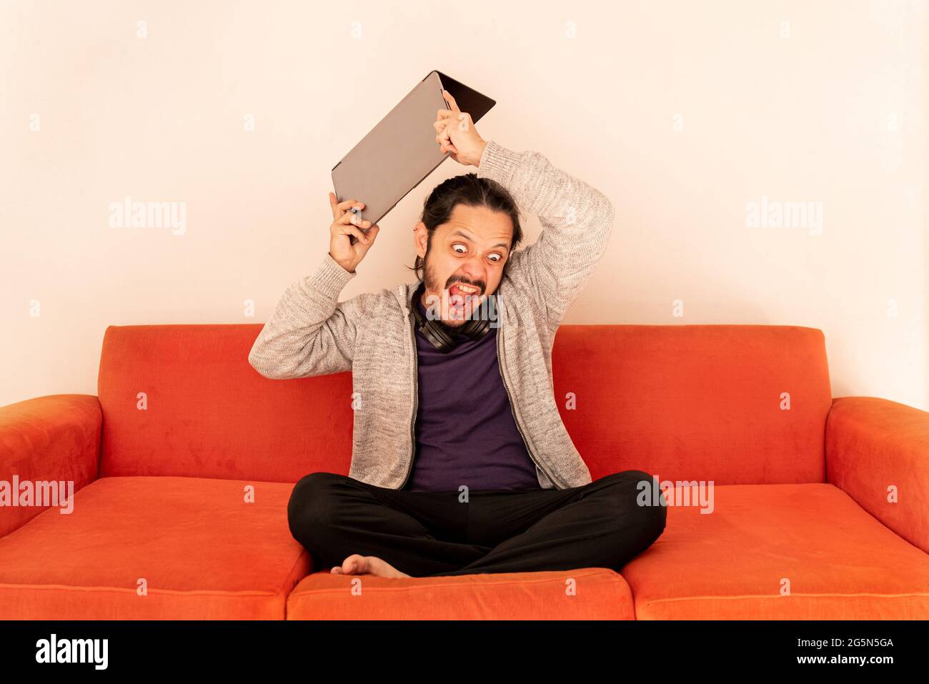 Young man angry with rage throwing the computer, sitting on an orange