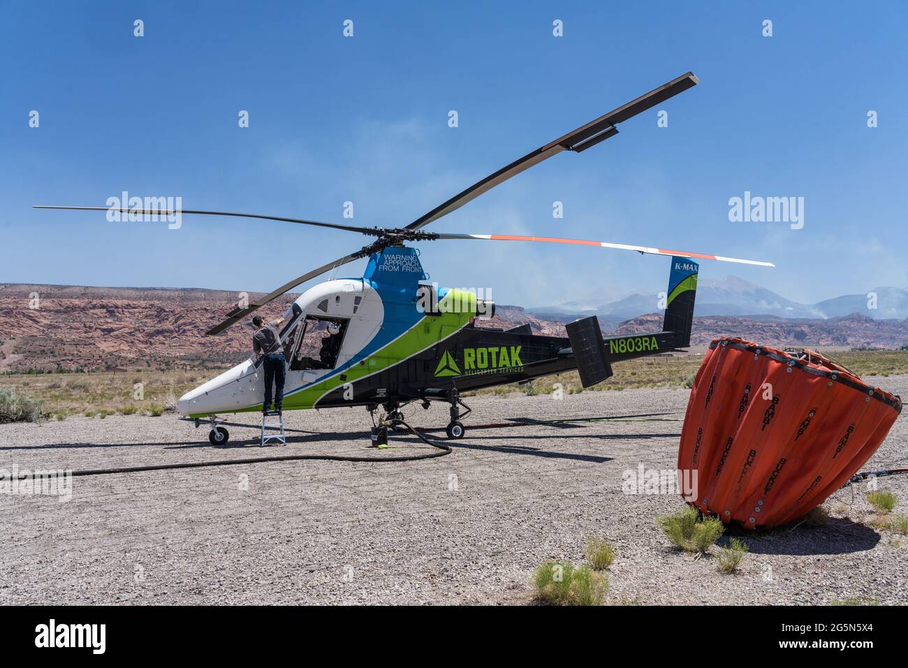 A Kaman K-Max K-1200 firefighting helicopter preparing to take off to fight a wildfire in Utah.  In the foreground is a 700 gallon external water heli Stock Photo