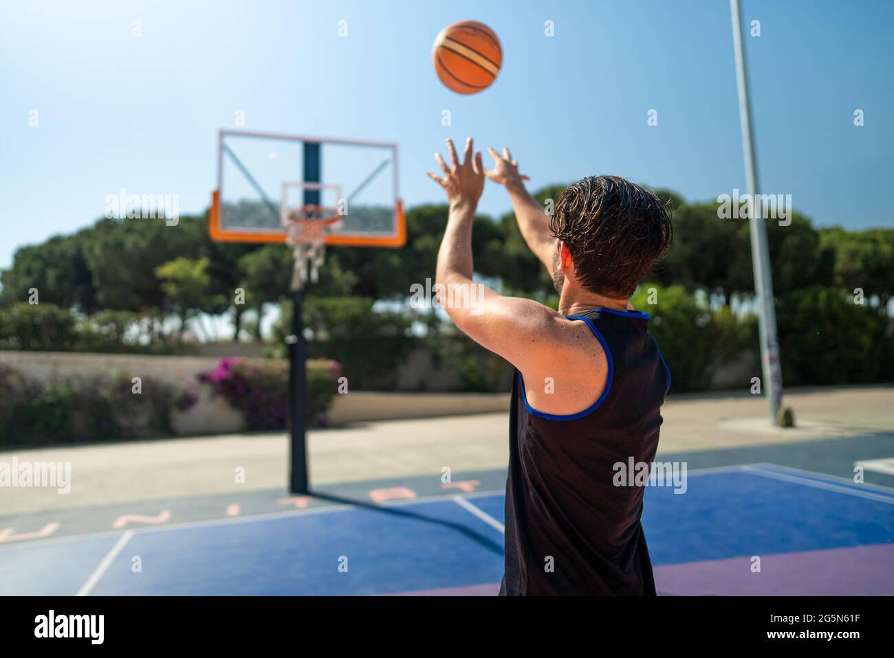 Male sportsman playing basketball throwing the ball at playground, back