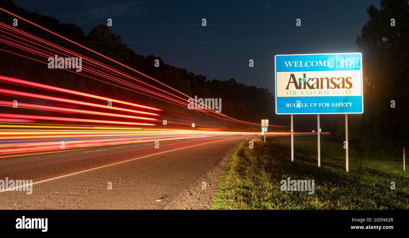 The sign says welcome to Arkansas is lit up by a passing semi truck Stock Photo
