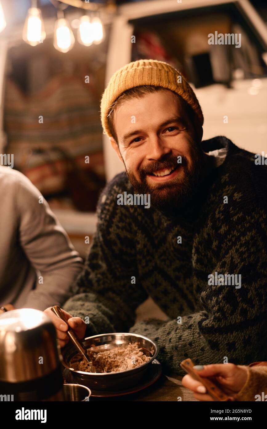 Young bearded man smiling at camera while having dinner on a picnic outdoors Stock Photo