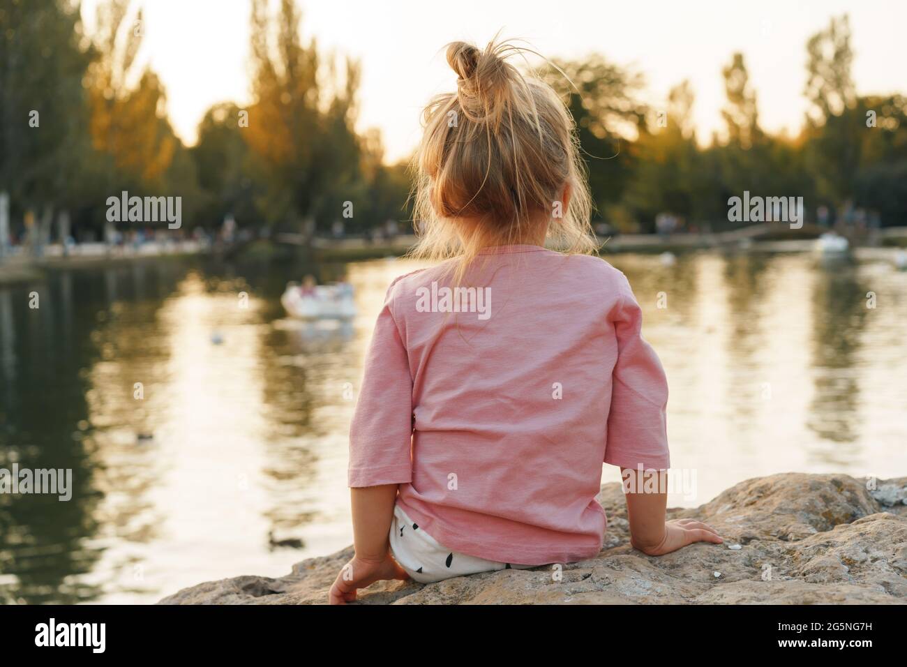 Little girl sitting on a huge stone in park near the lake Stock Photo ...