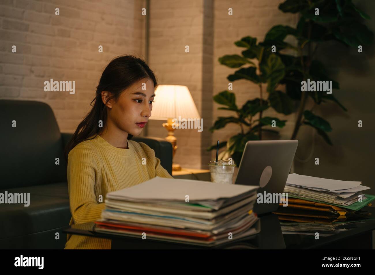 Young serious and focused Asian female entrepreneur working on laptop till late night on laptop with files while finishing project for deadline at home Stock Photo