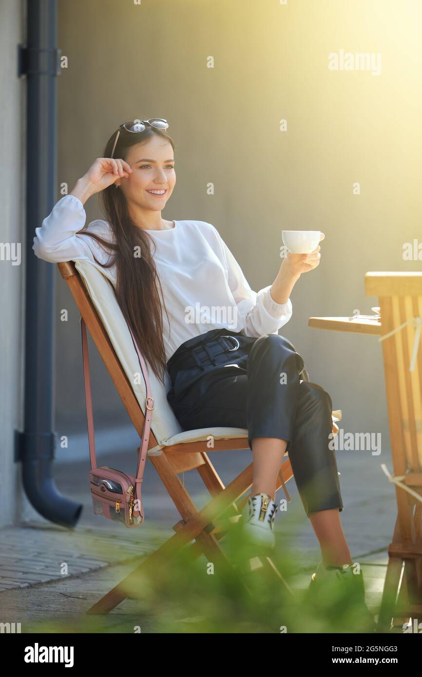 Happy young woman sitting on the terrace of the cafe in sunny day and ...
