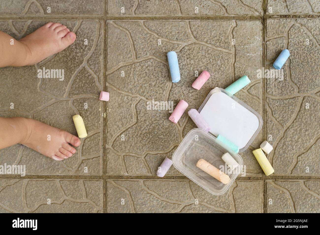 Flat lay pieces of colors chalk on the floor and toddler kid legs Stock Photo