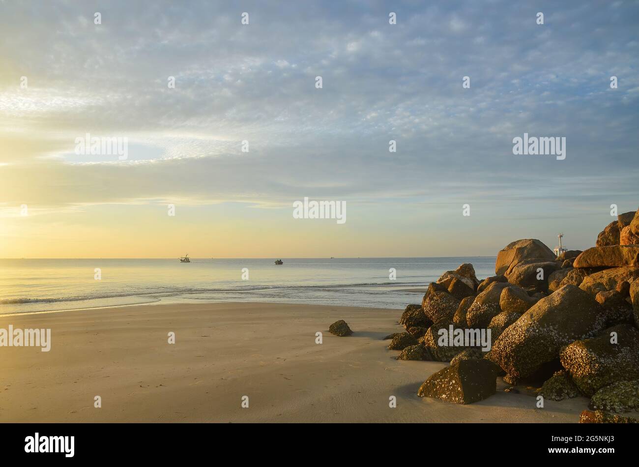 Colourful glowing pastel cirrostratus cloudy tropical beach sunrise seascape. Waterfront at dawn featuring a rock outcrop. Huay Yang, Thailand. Stock Photo