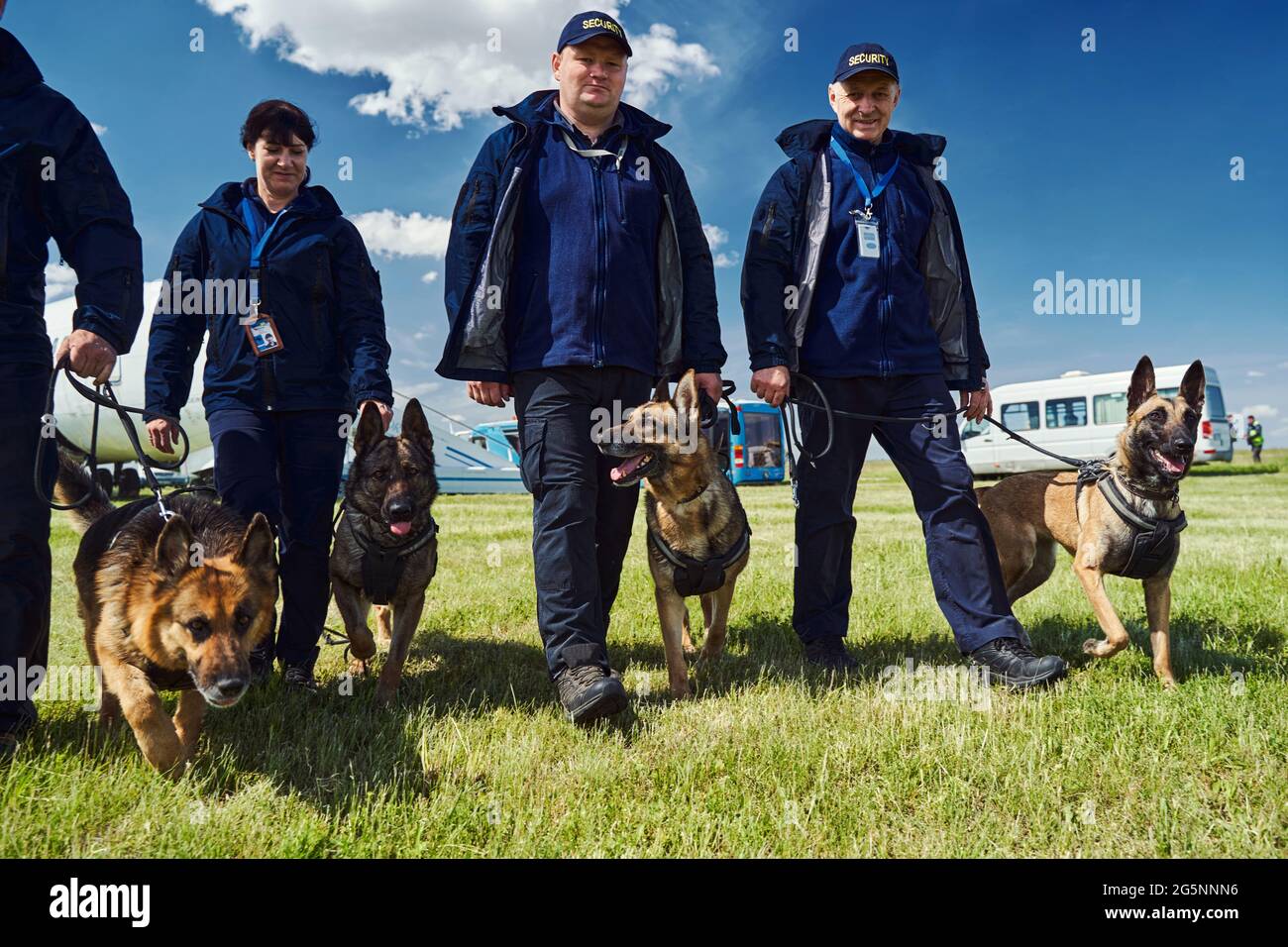 Cheerful security officers with detection dogs walking down airfield