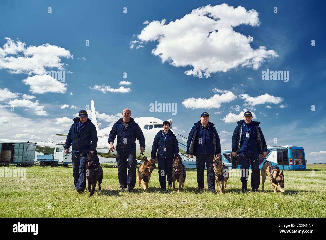 Security officers with detection dogs walking down airfield Stock Photo