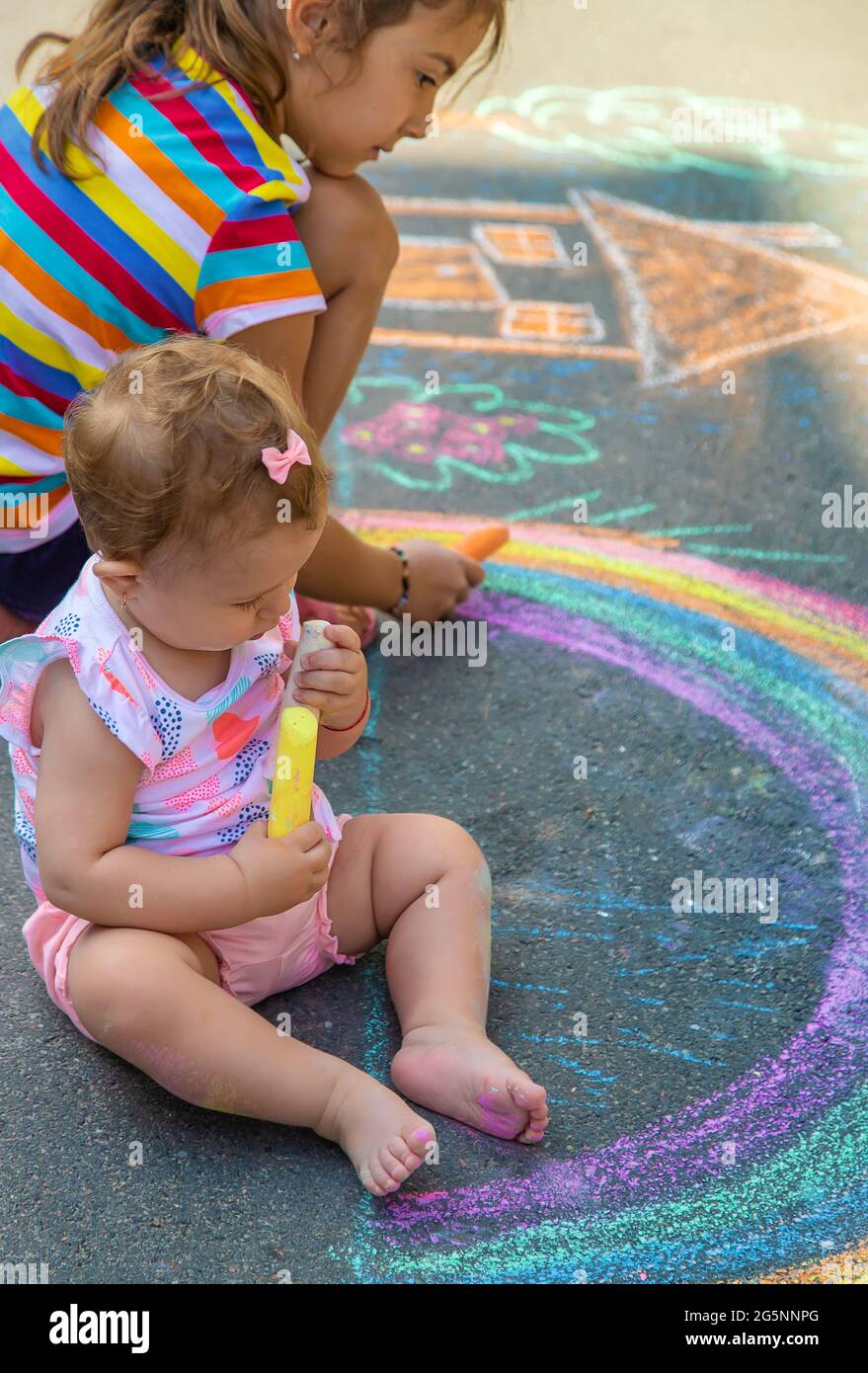 The child draws a house and a rainbow on the asphalt with chalk ...