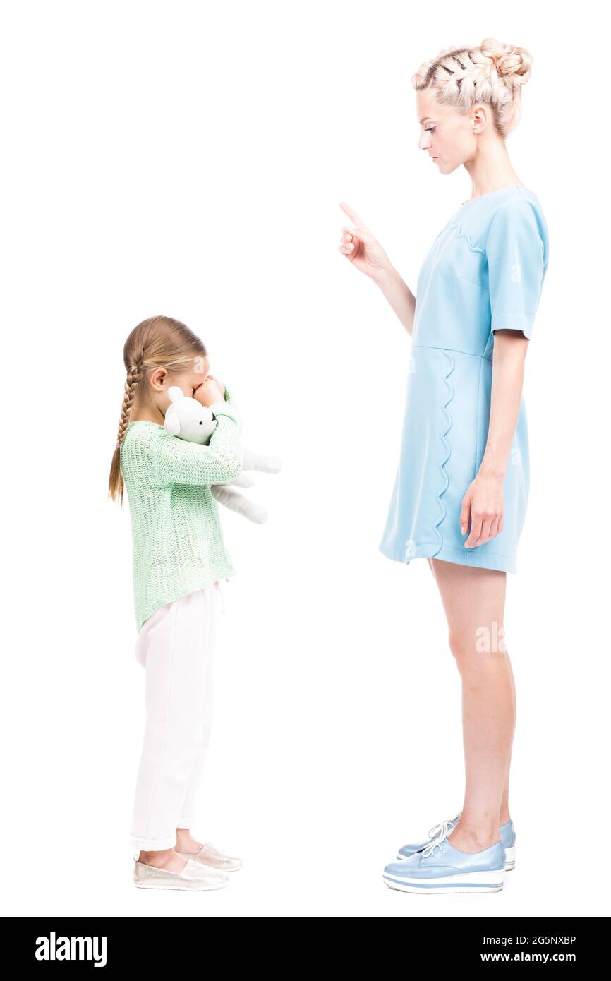 Vertical full length isolated side view shot of young adult woman scolding her daughter for being naughty, white background Stock Photo