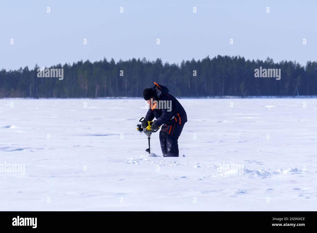 man drills holes in the ice for ice fishing with an electric auger. selective focus Stock Photo