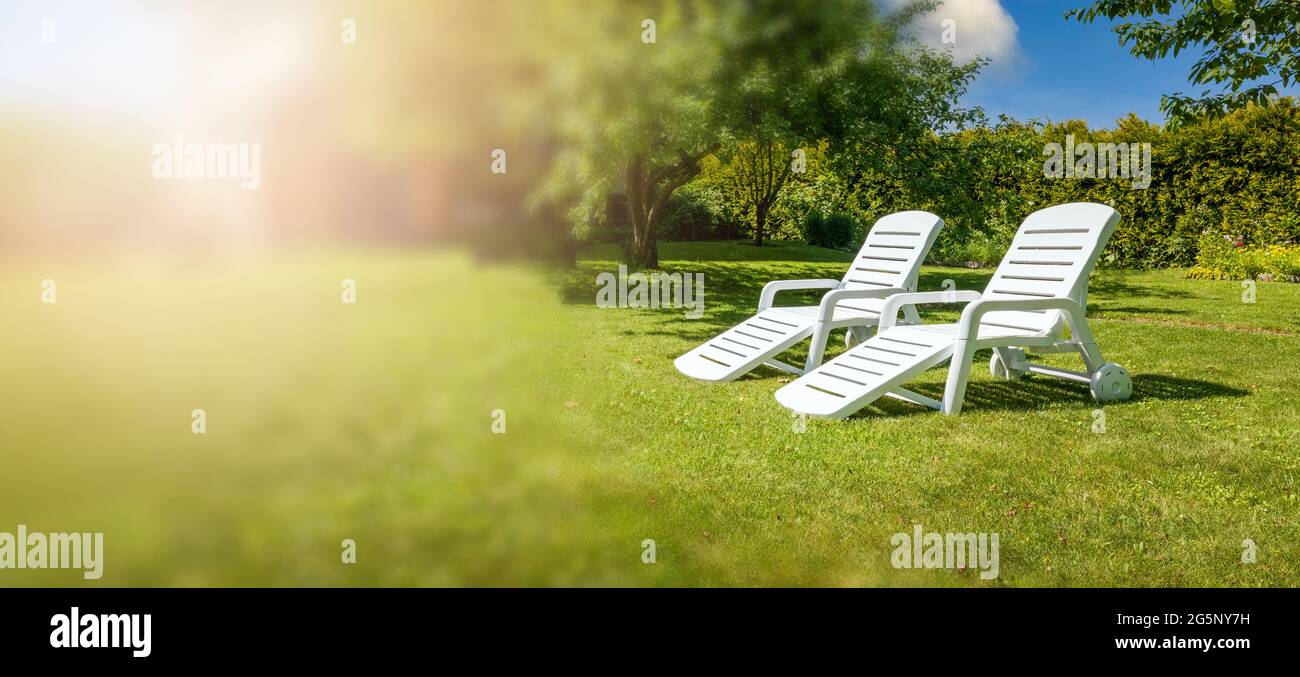 garden furniture - white loungers on green grass in backyard. copy space Stock Photo