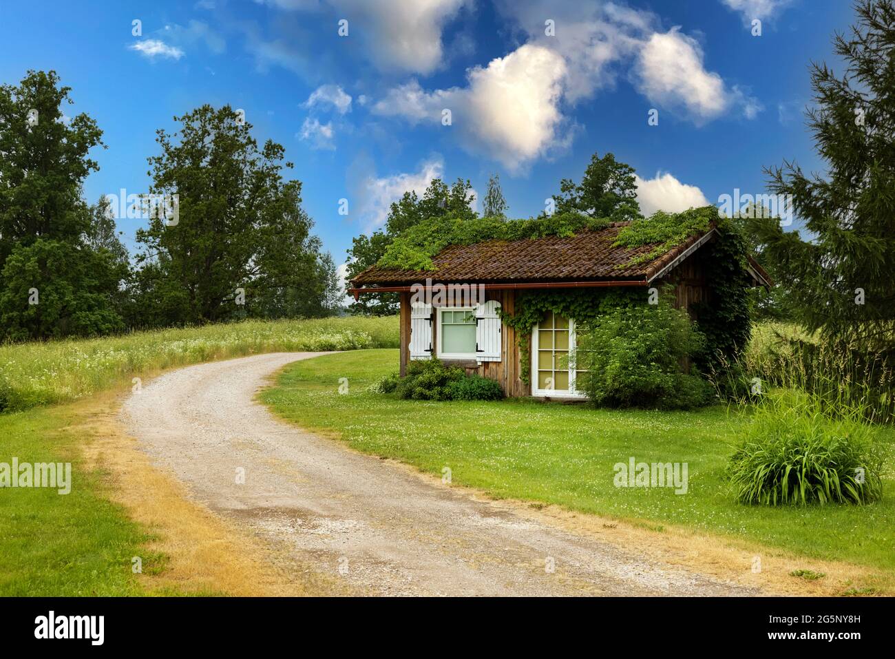 small wooden lodge and country road in countryside. idyllic landscape Stock Photo