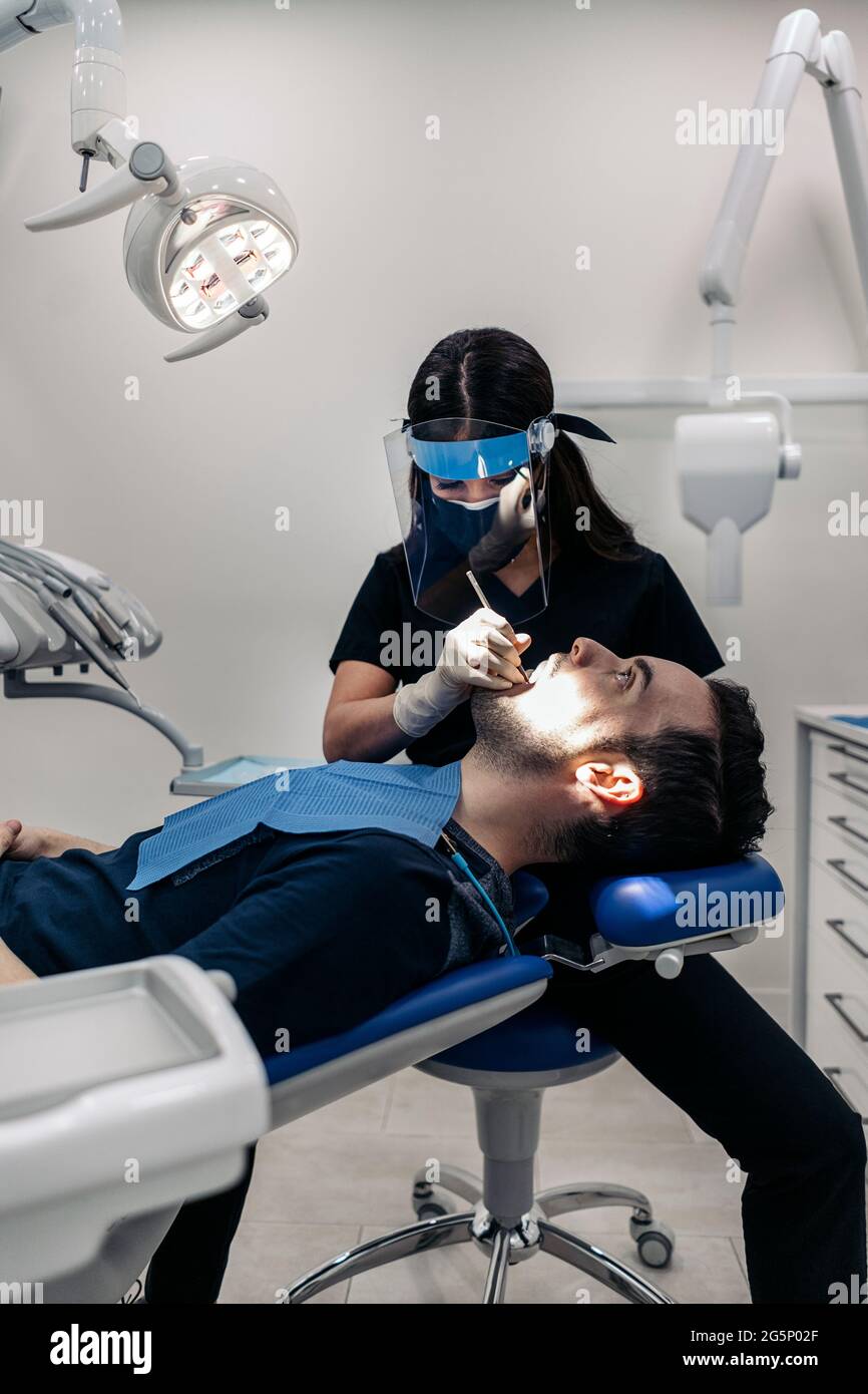 Female dentist wearing protective face mask working with young man