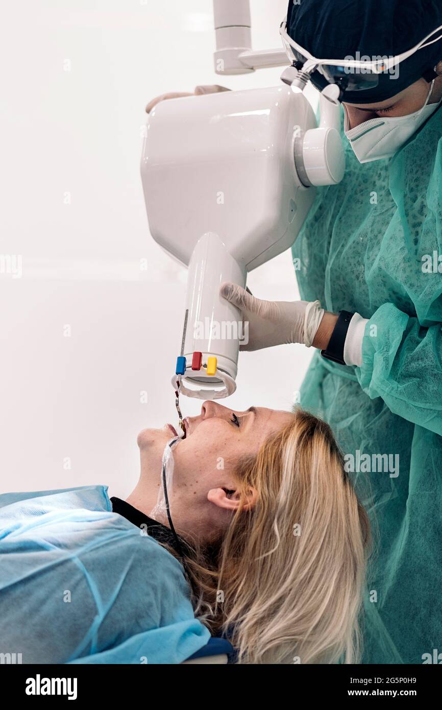 Adult woman lying in dental chair receiving dental treatment. The dentist is wearing face mask