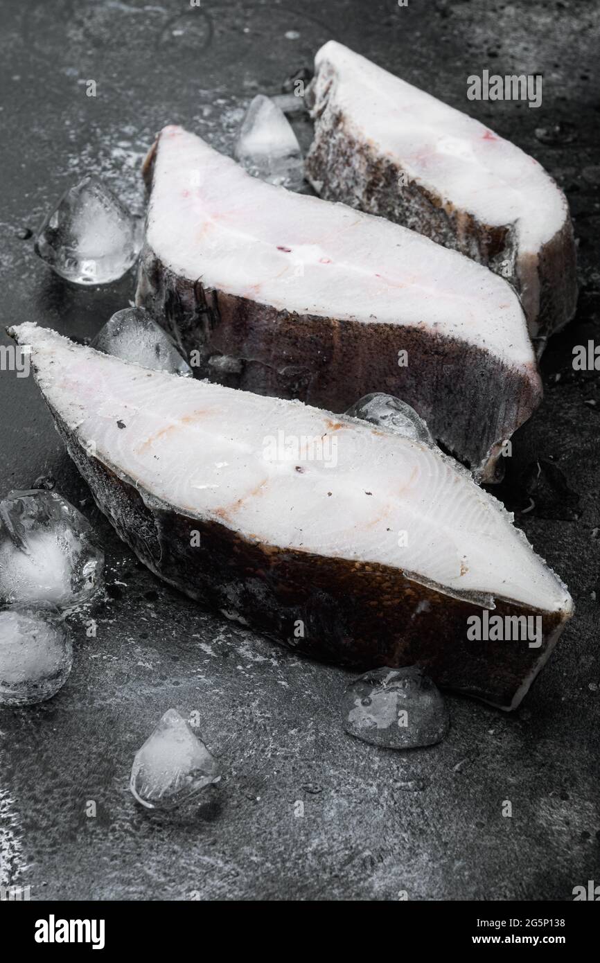 Frozen halibut steak set, on black dark stone table background Stock