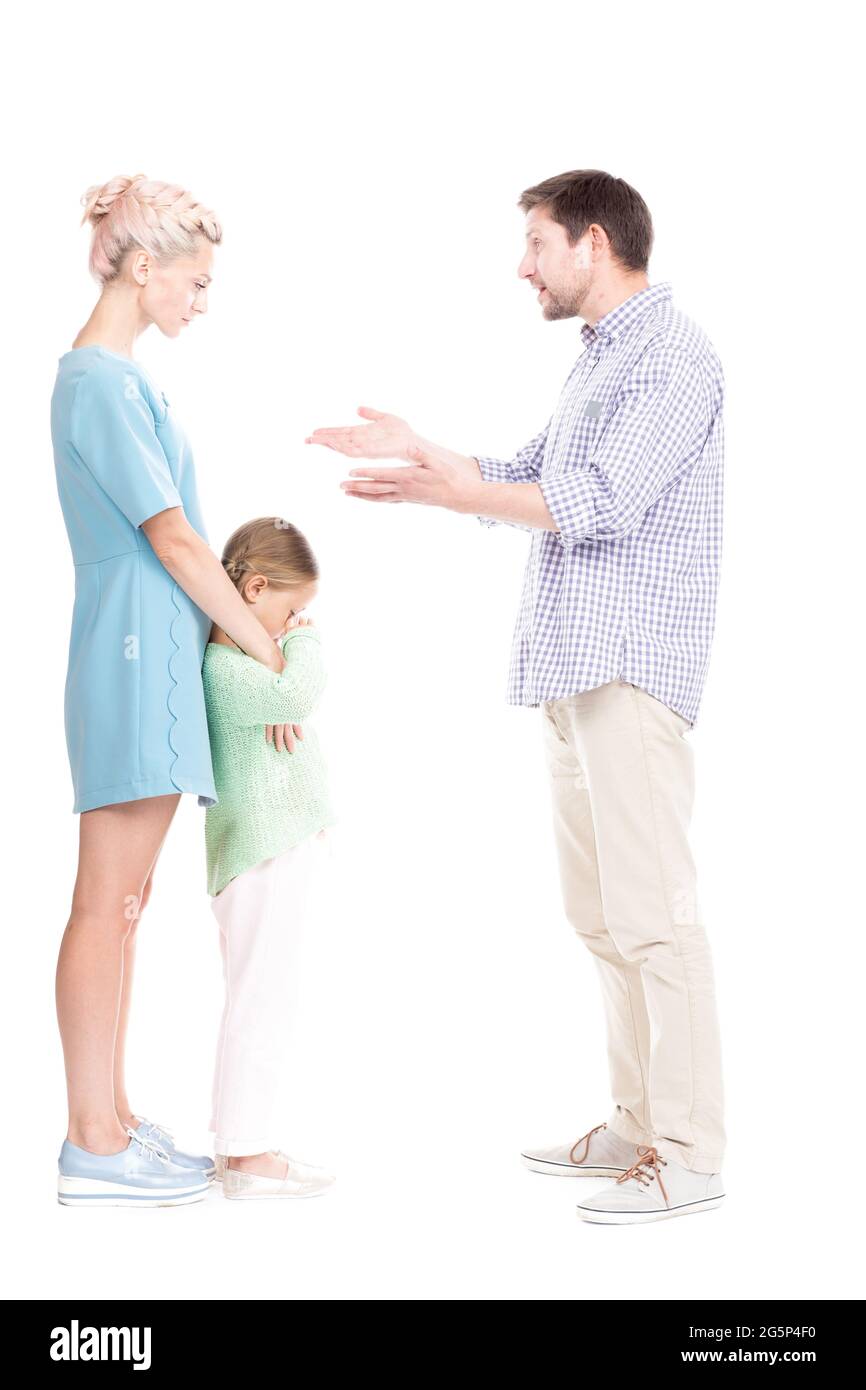 Vertical full length side view studio shot of husband and wife having conflict quarrelling, their daughter feeling sad about it, white background Stock Photo