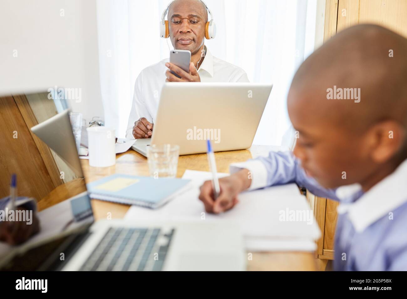 Father at video conference and son online at home computer at homeschooling in the living room Stock Photo