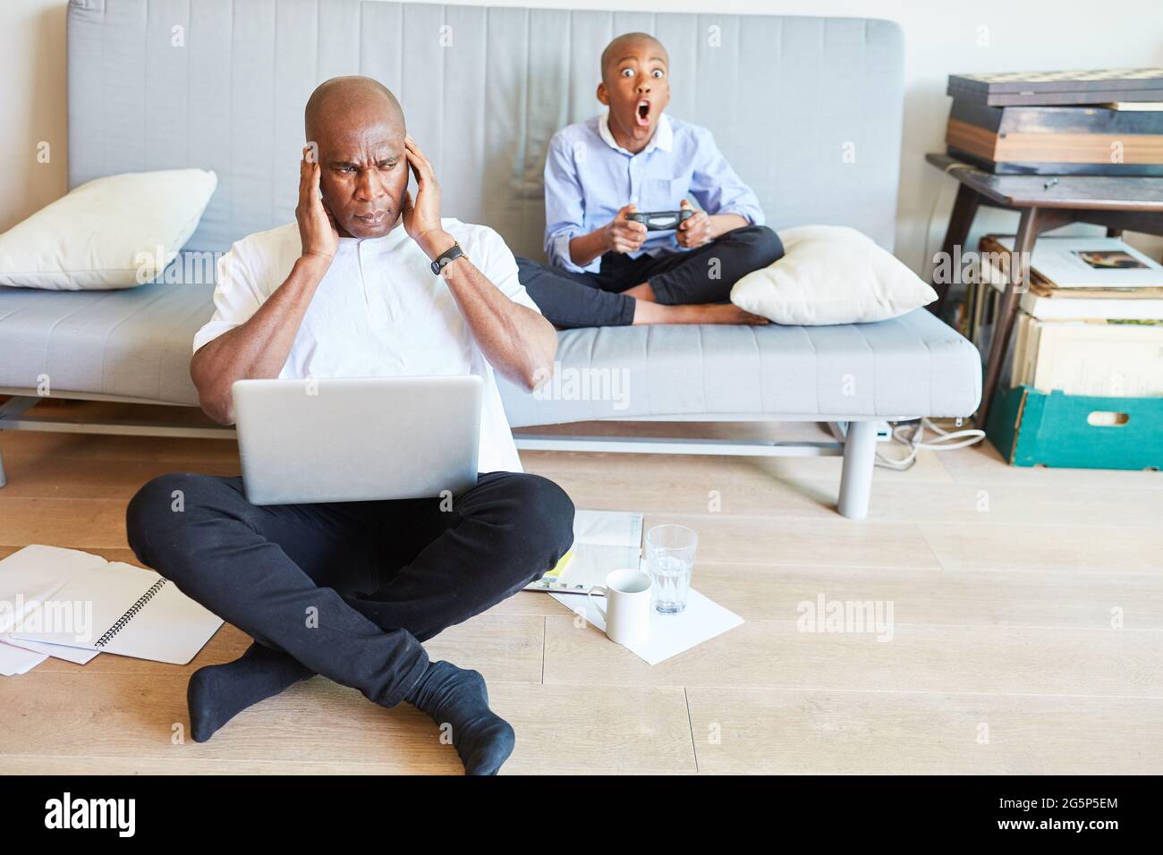 Business man stressed by noise in the home office because of child playing video game on the sofa Stock Photo