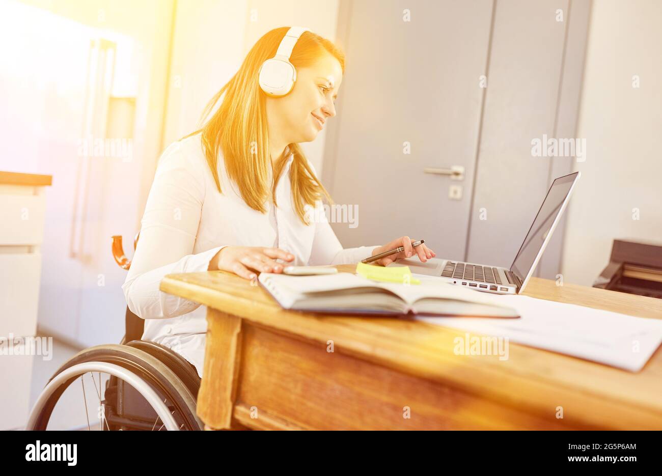Disabled young woman in wheelchair at computer while distance learning at home Stock Photo