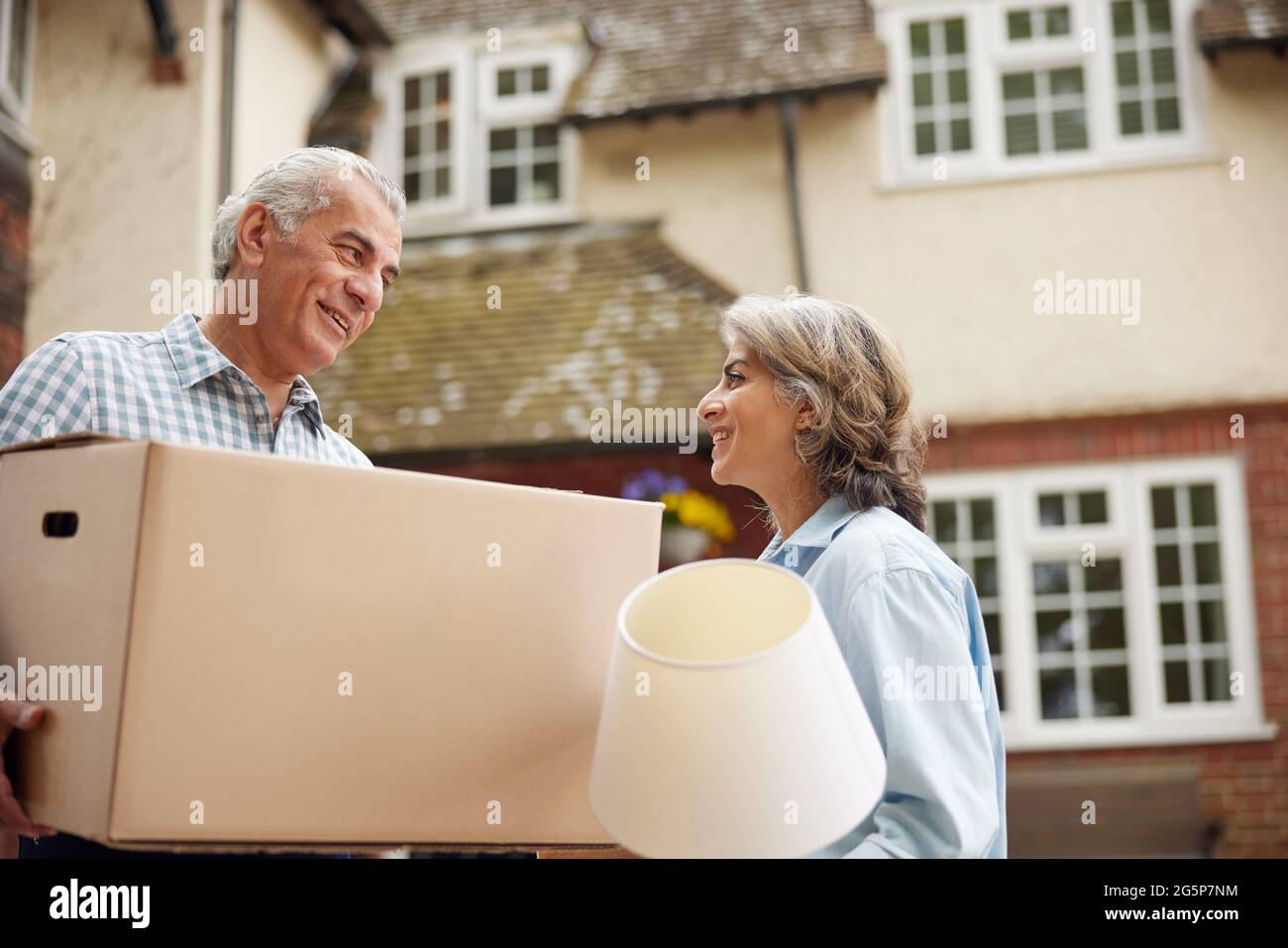 Mature Couple Carrying Boxes On Moving Day In Front Of Dream Home Stock Photo