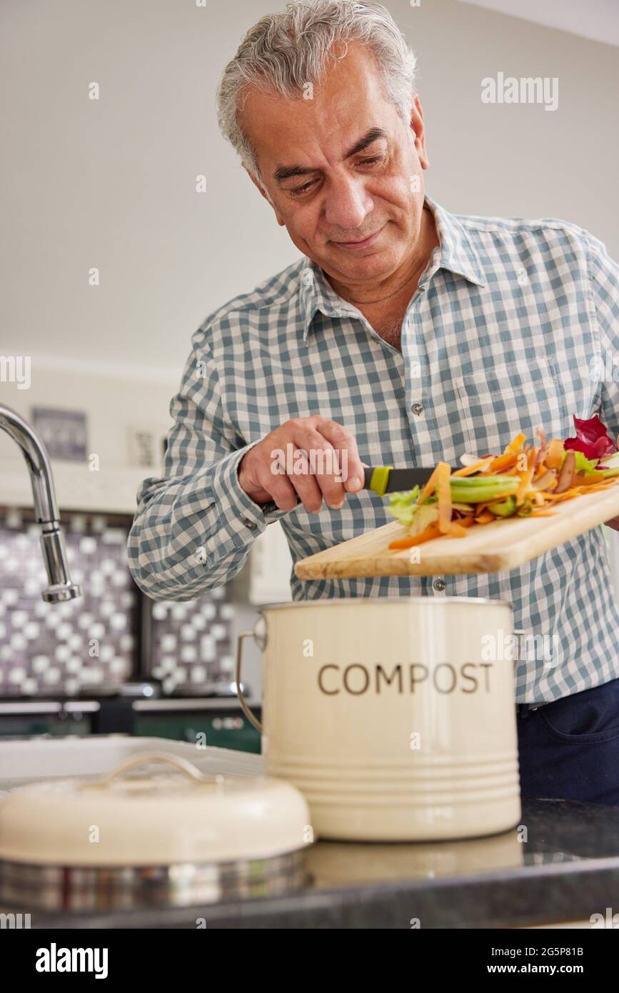 Mature Man In Kitchen Making Compost Scraping Vegetable Leftovers Into Bin Stock Photo