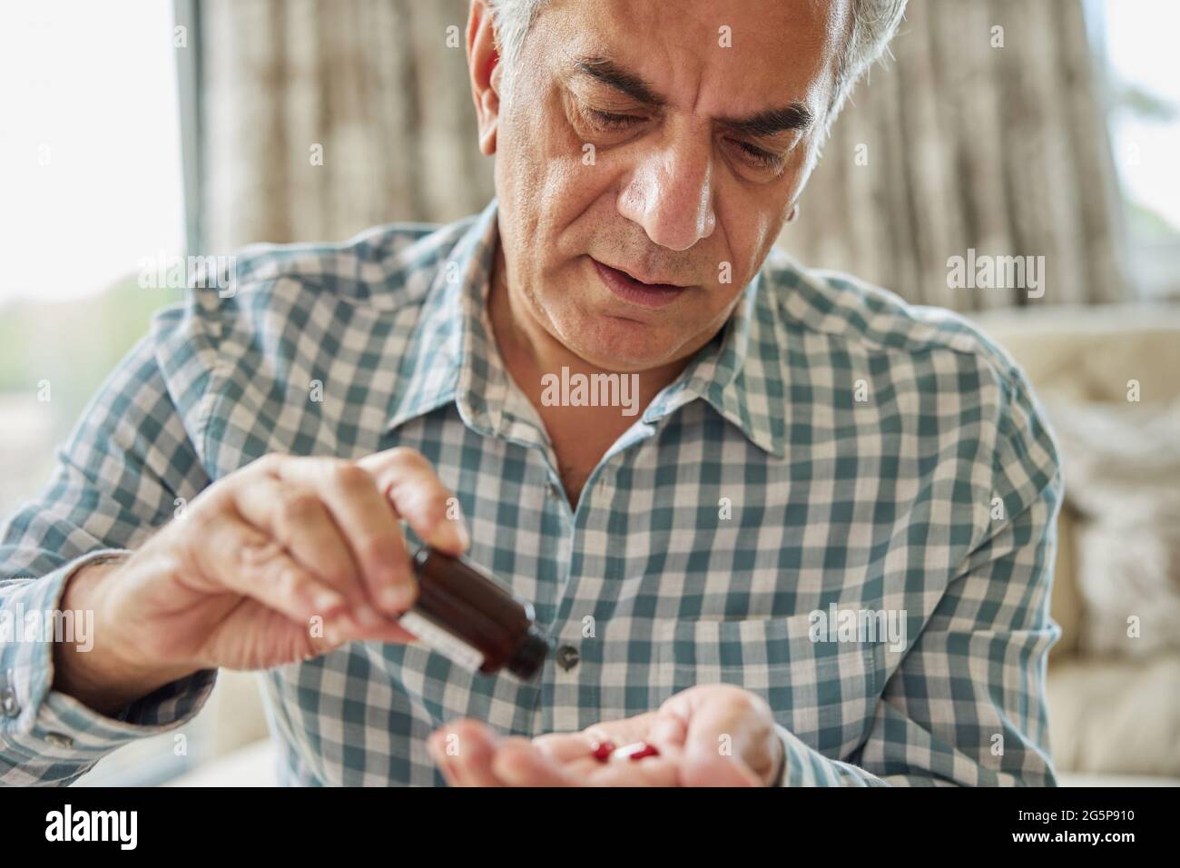 Mature Man Sitting On Sofa At Home Taking Medication Stock Photo