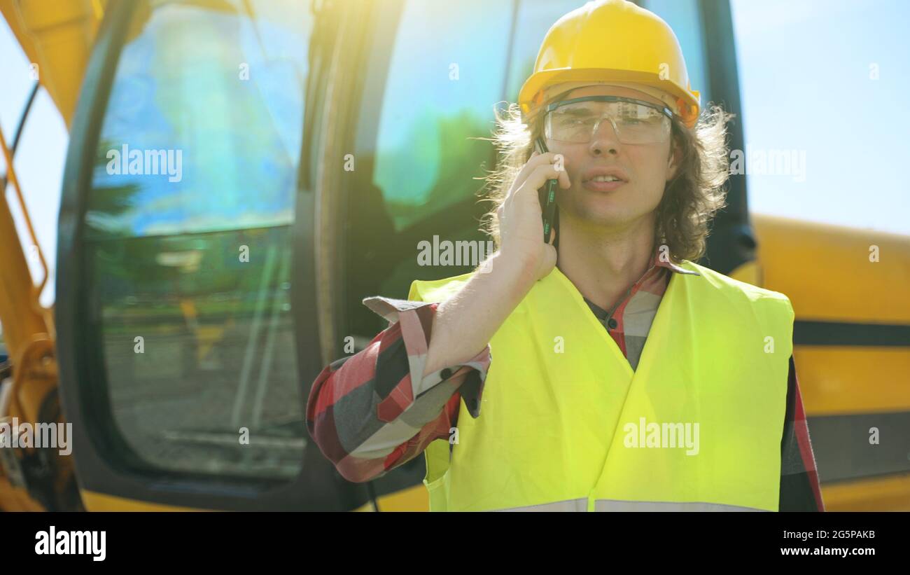 Excavator operator in hard hat talking by smartphone. Stock Photo
