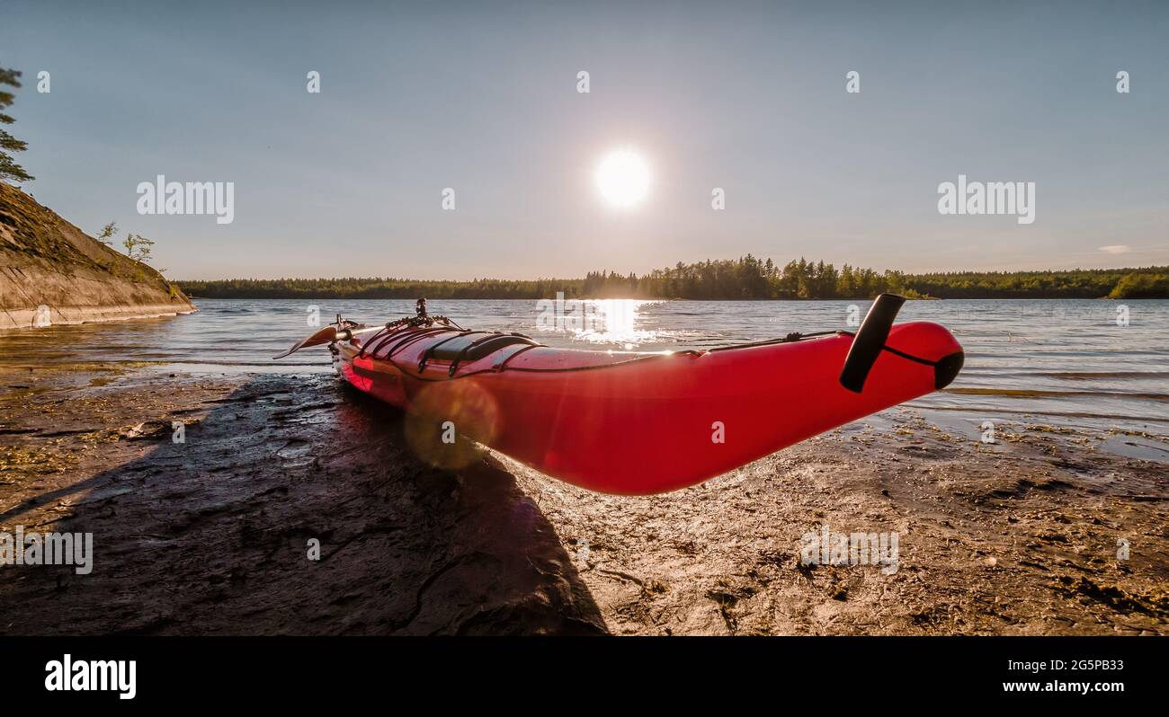 Close up view of red kayak at wet river coastline, stony slope, sunny summer day, outdoor sport activity. Umea river delta, Vasterbotten county, Swede Stock Photo