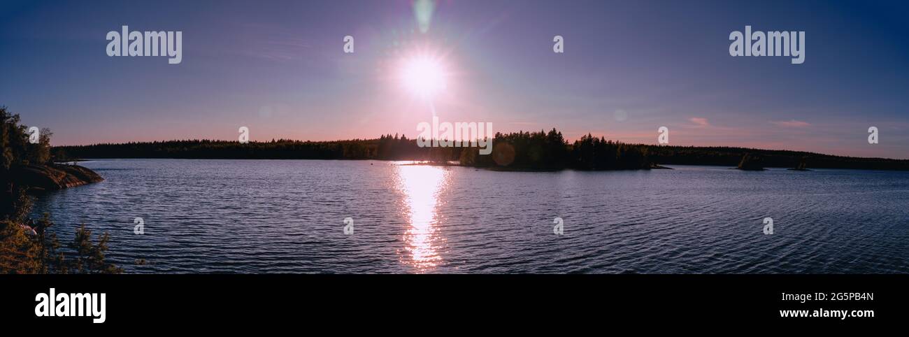 Aerial panoramic Sunset photo of Umea river with few small islands, pine tree forest on coast line, Sun path across the river, lens flares and Sun ray Stock Photo