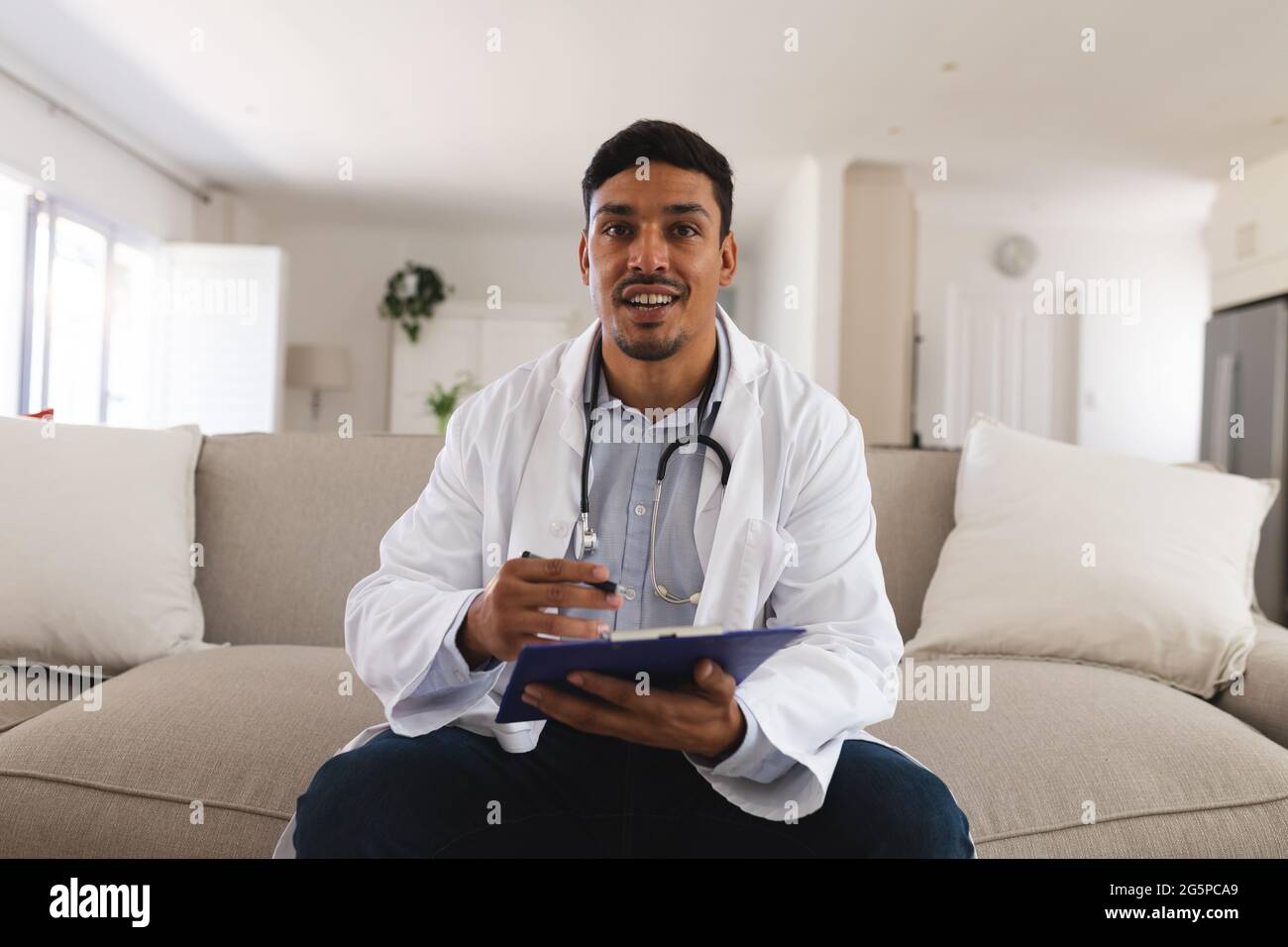 Hispanic male doctor sitting on couch talking during consultation video