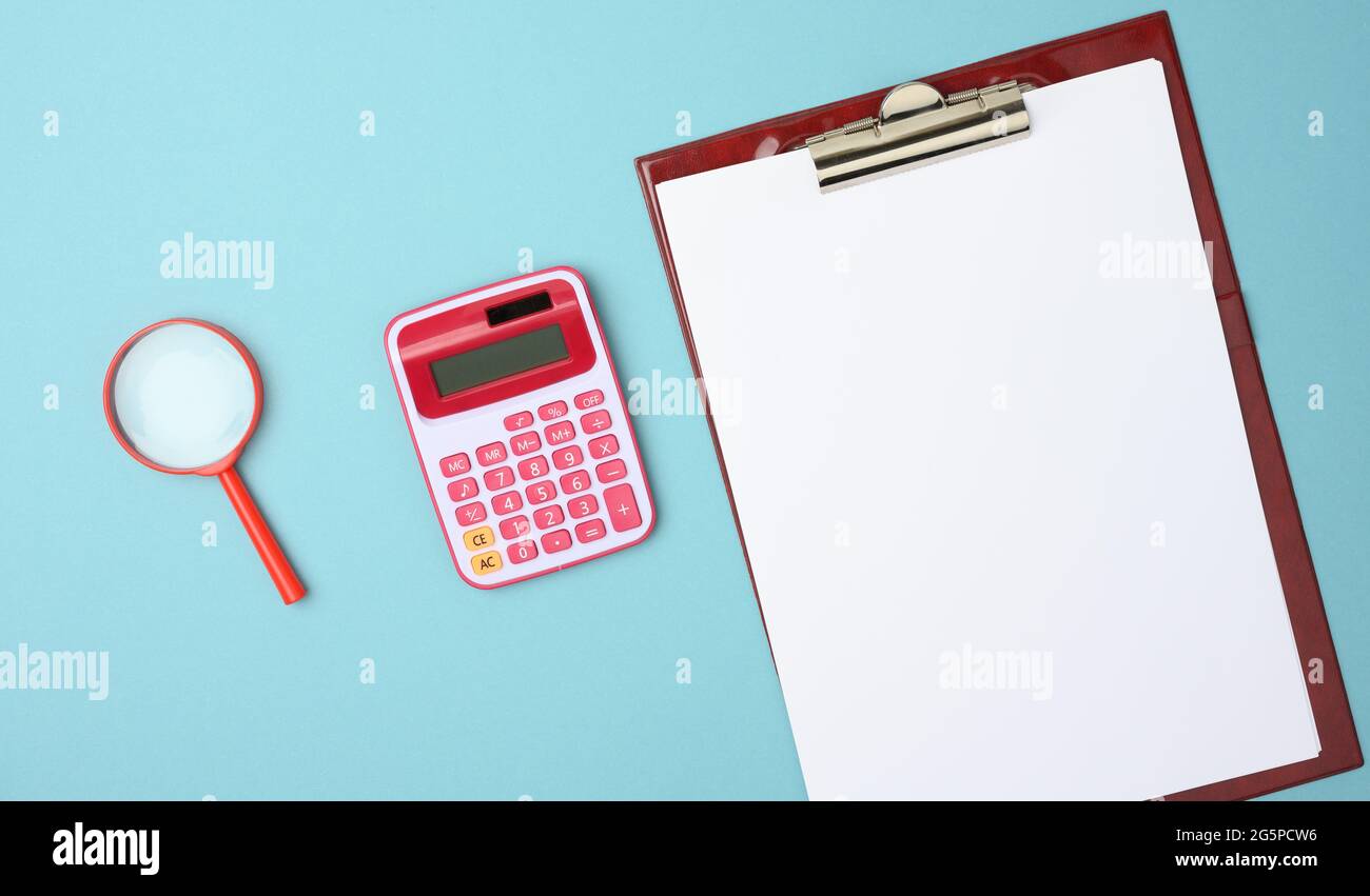 pink calculator, folder with blank white sheets and black magnifier on a blue background, top view Stock Photo