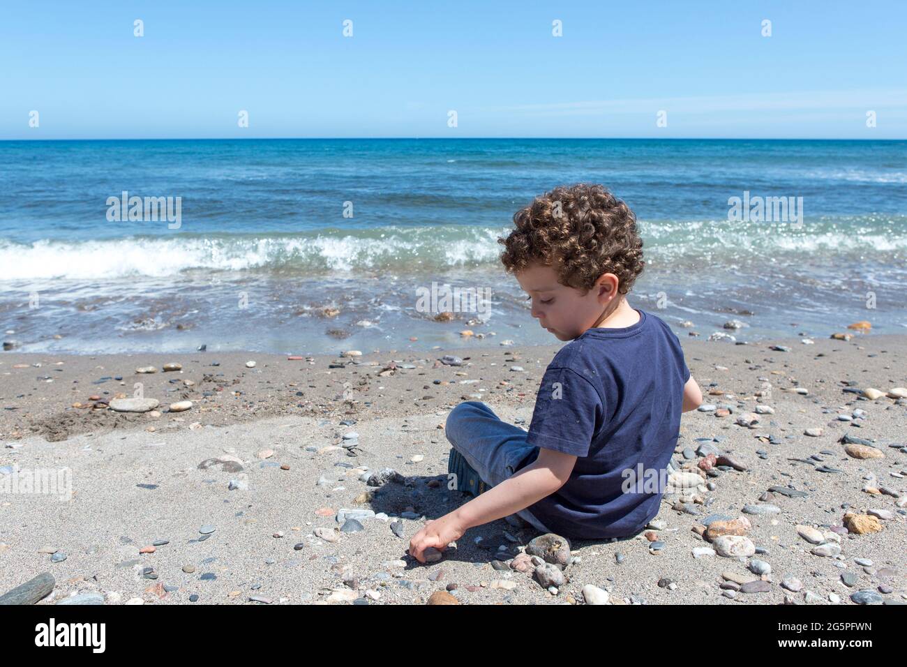small 4-5 year old playing with the stones that are on the shore of the beach Stock Photo