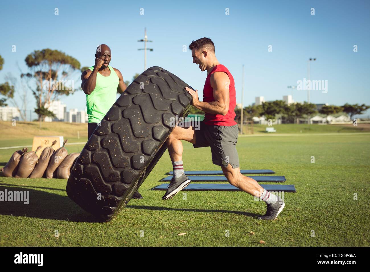 Diverse fit man and trainer exercising outdoors, encouraging and lifting heavy tyre Stock Photo