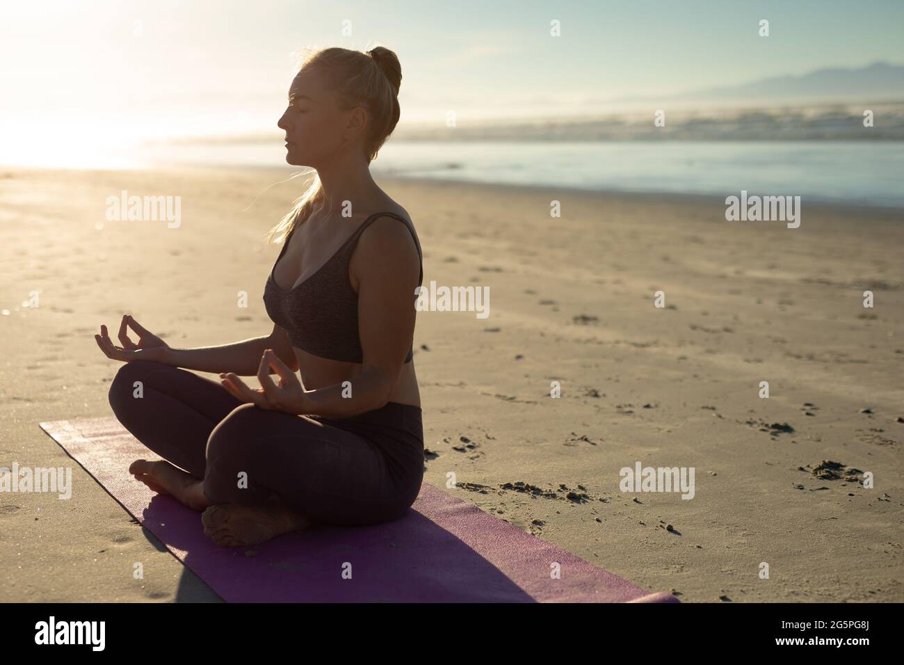 Caucasian woman practicing yoga, sitting meditating at the beach Stock Photo