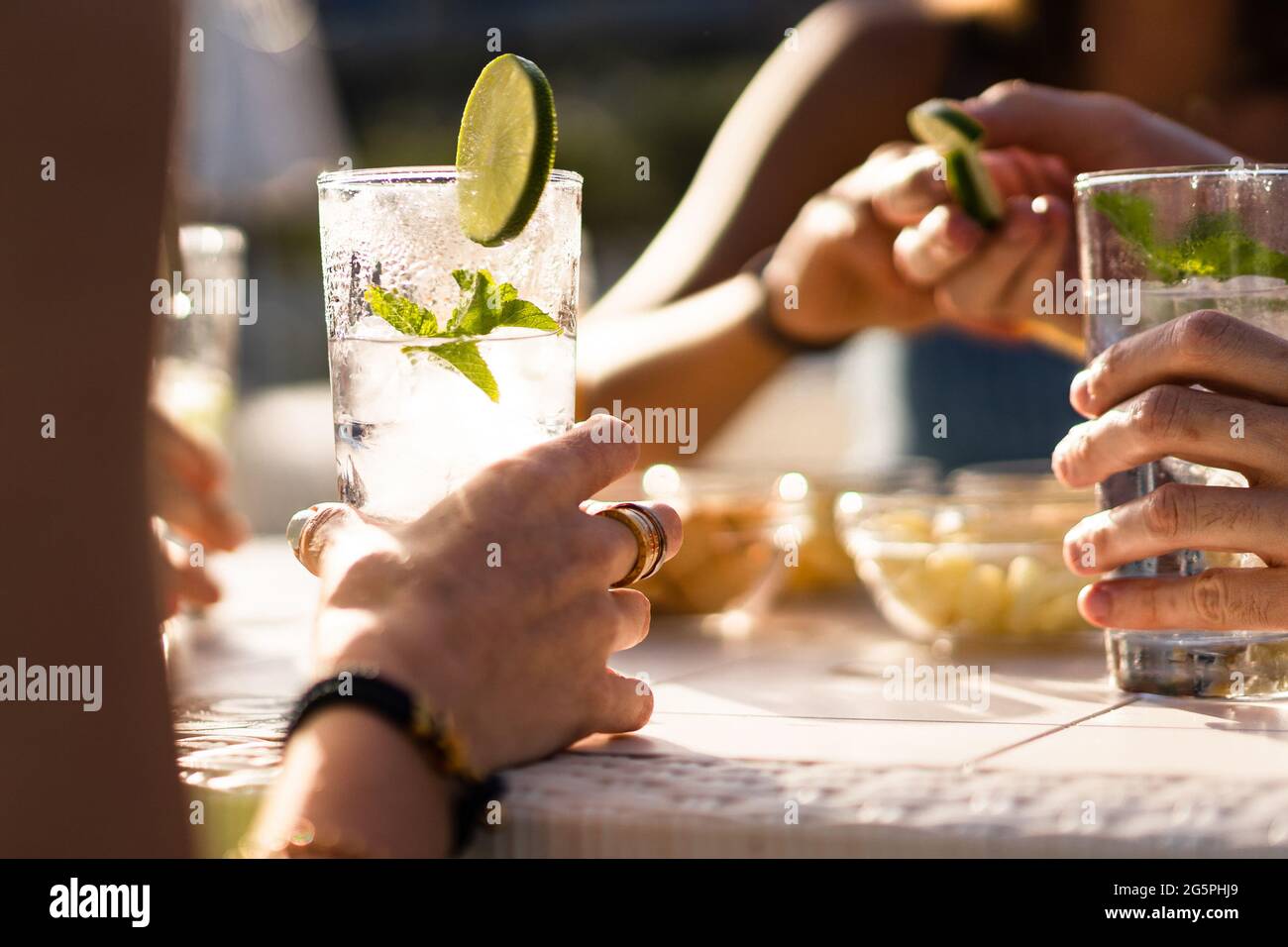 Hands holding a fresh alcoholic long drink cocktail on a table. Gathering of friends in an outdoor pub in the summer. Stock Photo