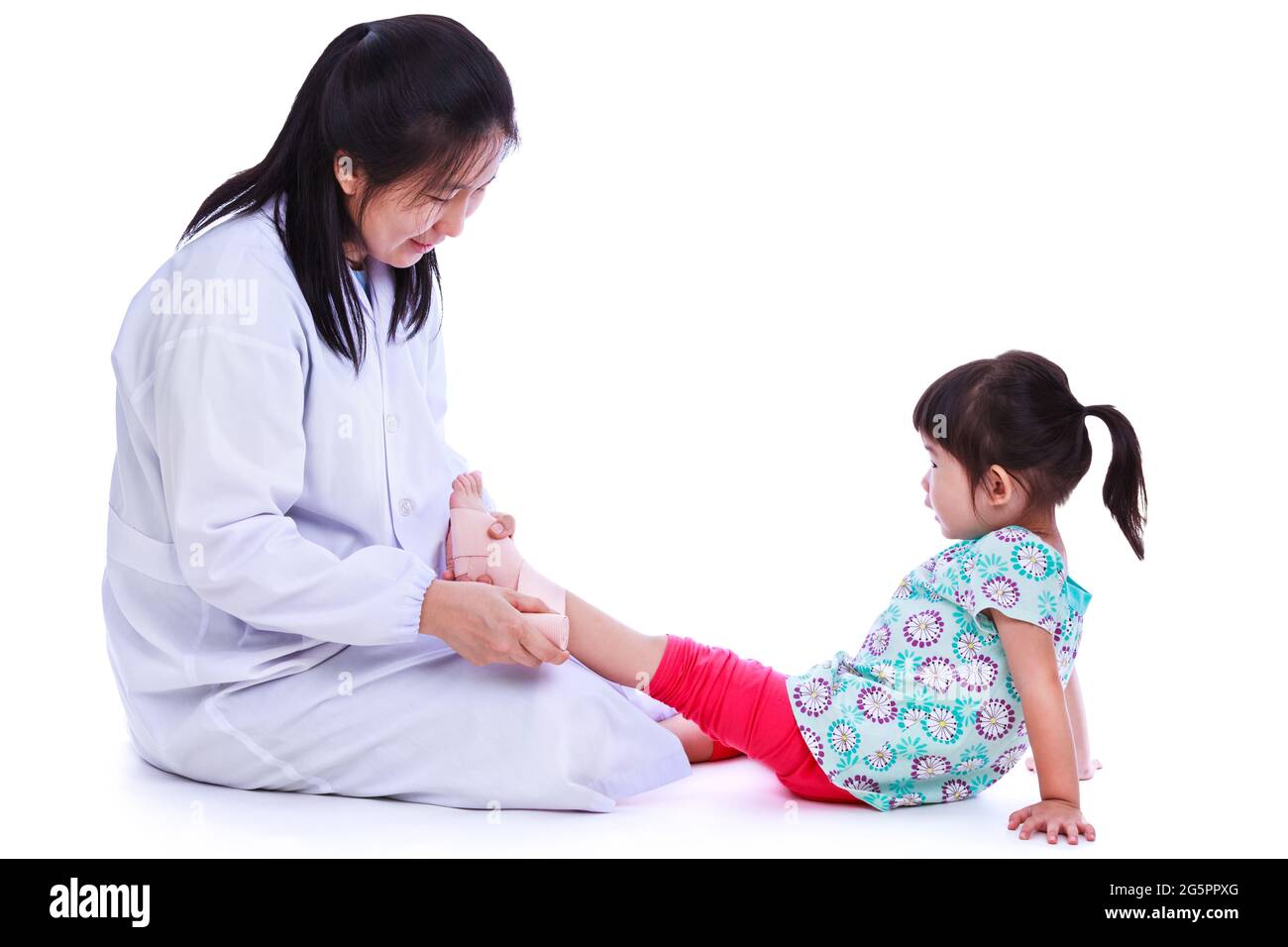 Concept photo of children health and medical care. Doctor give first aid with bandaging at girl's ankle trauma. Studio shot. Isolated on white backgro Stock Photo