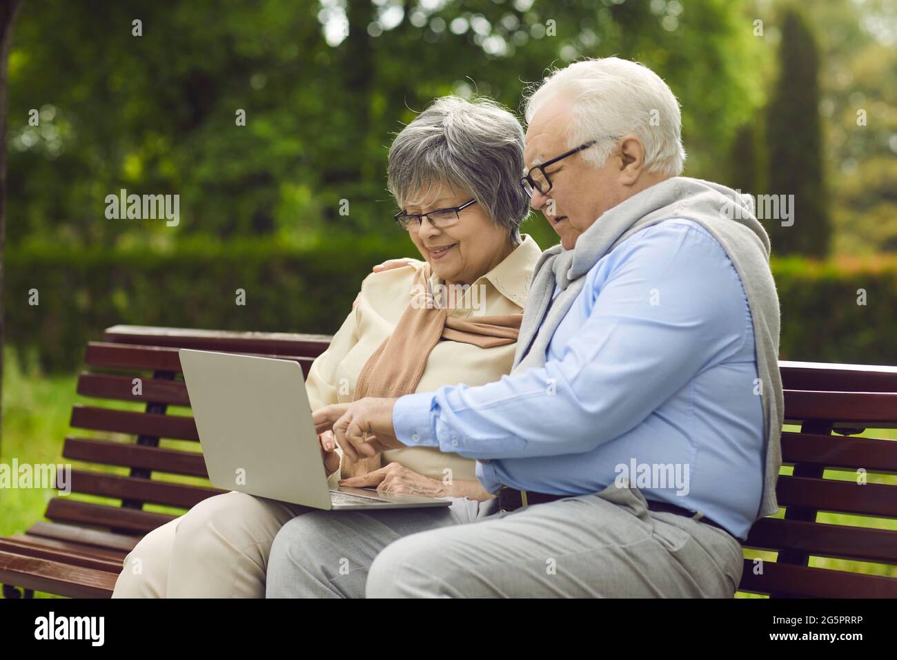 Happy senior couple using a laptop computer while sitting on a park bench together Stock Photo