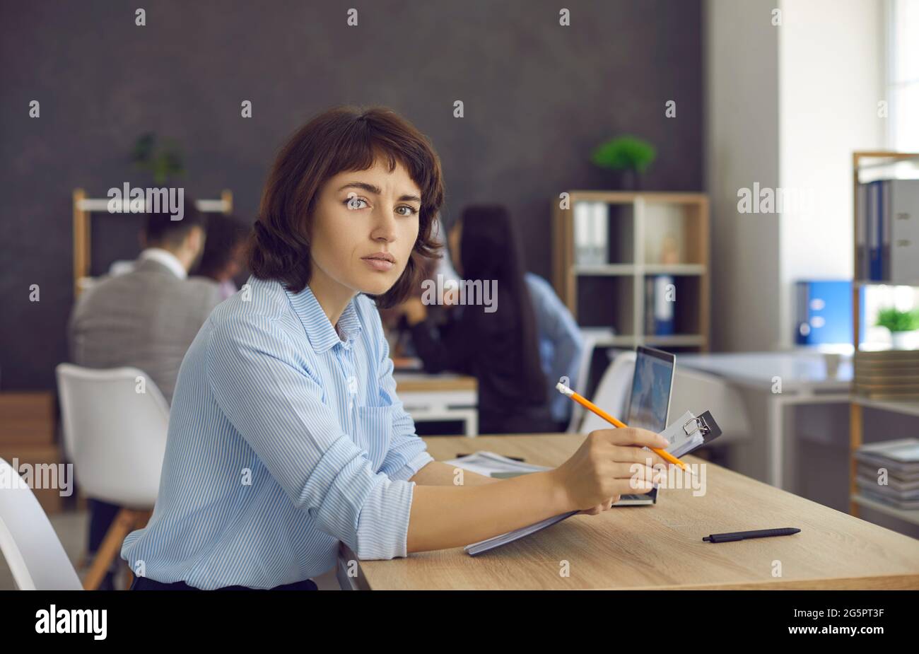 Portrait of businesswoman sitting at office desk, holding clipboard and looking at camera Stock Photo