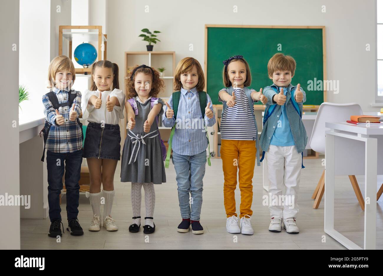 Happy smiling little children showing thumbs up standing in school classroom Stock Photo