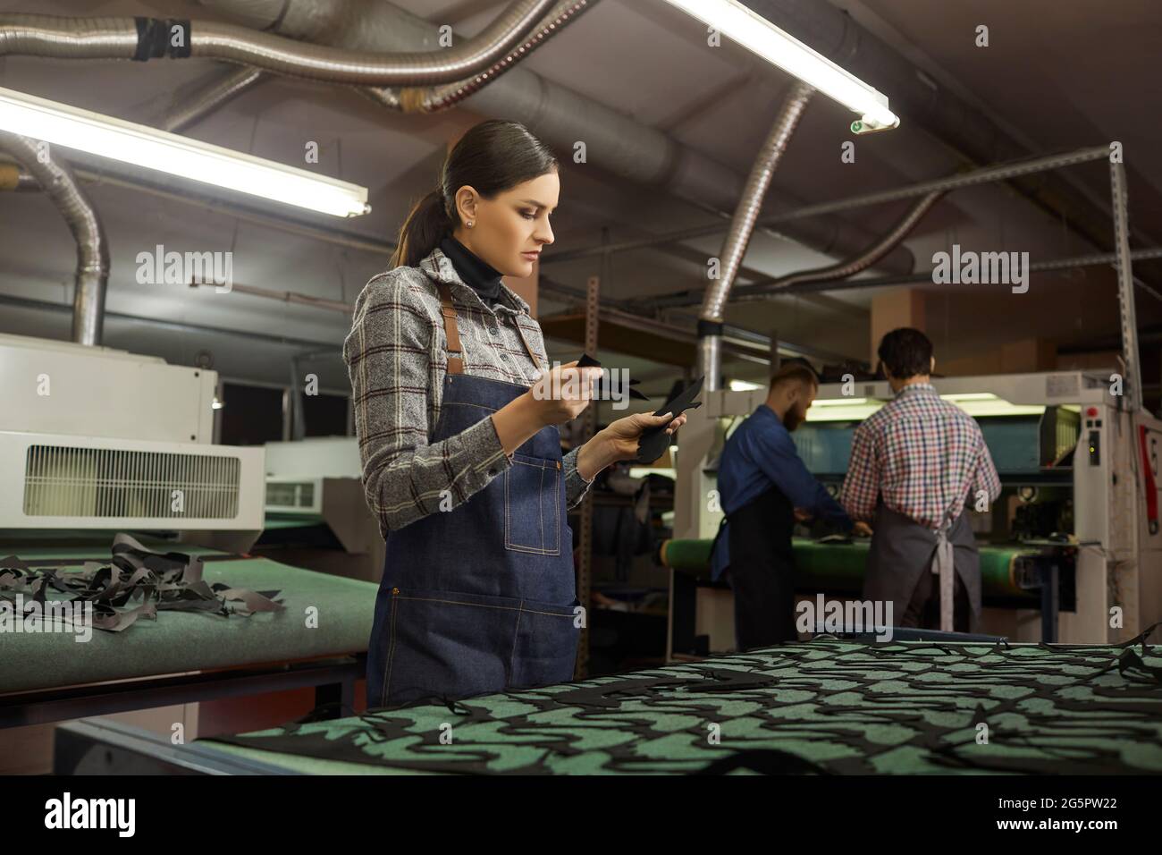 Concentrated young artisan holding leather pieces in shoemaking workshop Stock Photo