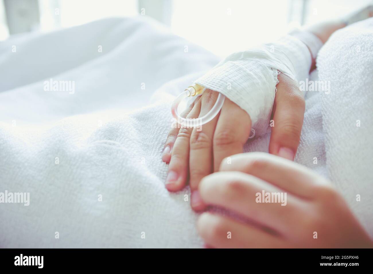 Close up of saline intravenous (iv) drip in a child's patient hand. Health care and people concept. Vintage tone. Stock Photo