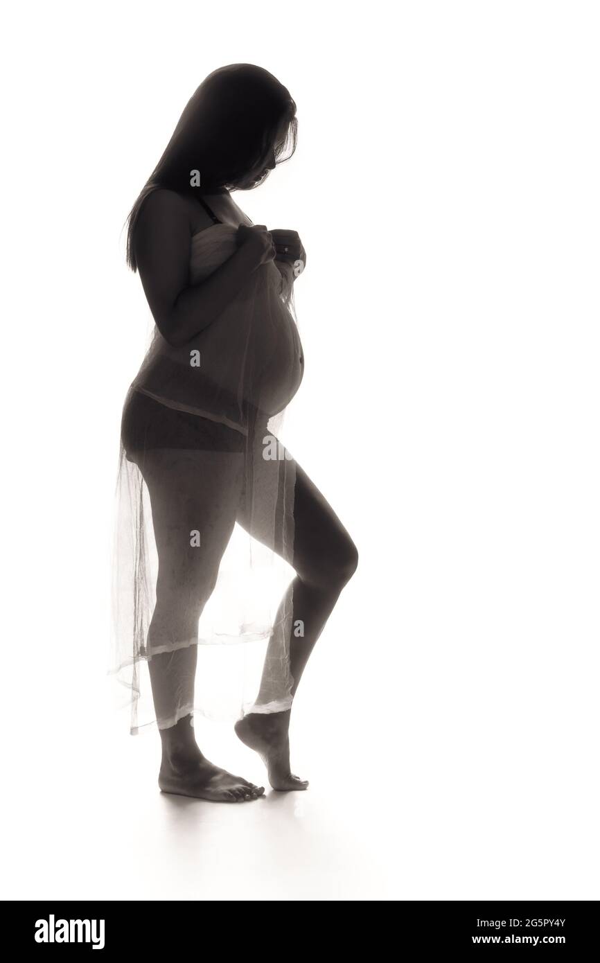 Backlit low key photo of a young pregnant woman. Stock Photo