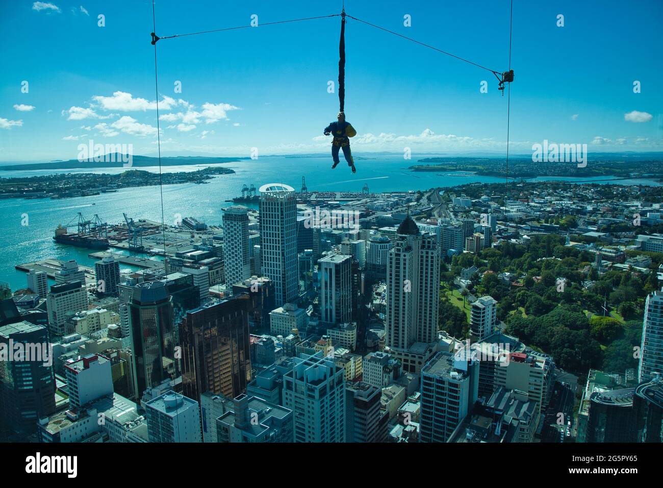 A person hangs in mid air just before doing a tethered sky fall from the Sky Tower in Auckland, North Island, New Zealand, with city buildings beyond Stock Photo
