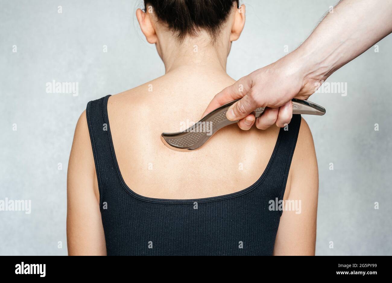 Instrument-assisted soft tissue mobilization, a woman receiving soft tissue treatment on her back with IASTM stainless steel tool Stock Photo