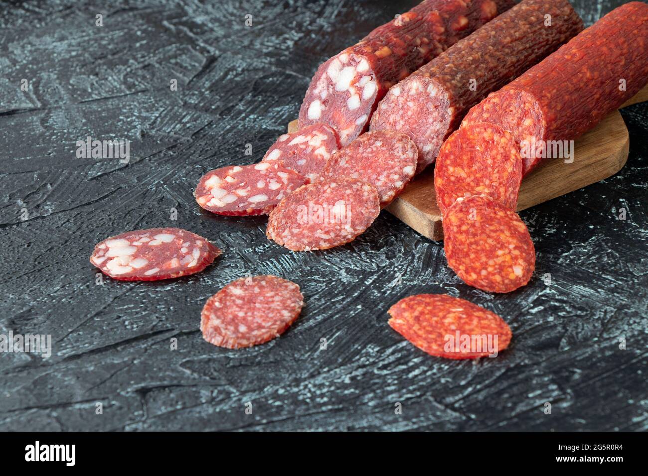 three kind of different sausages on a cutting board. Pieces of sausage cut into circles on a black background. Soft focus. Stock Photo