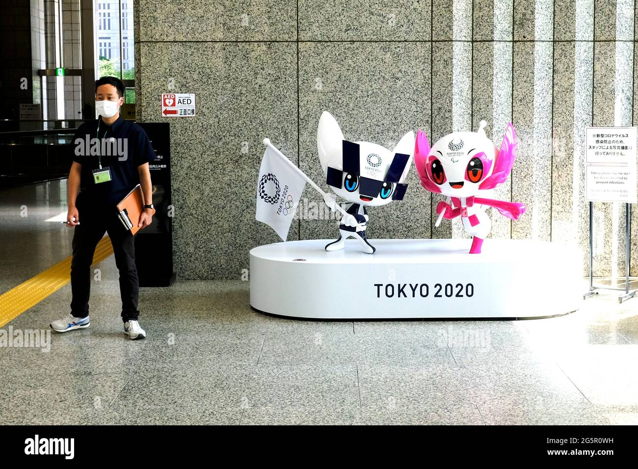 Tokyo, Japan. 29th June, 2021. A man wearing a mask stands next to official characters from the Olympic and Paralympic Games 2020 on display at the Tokyo Metropolitan Government in Tokyo. Credit: SOPA Images Limited/Alamy Live News Stock Photo